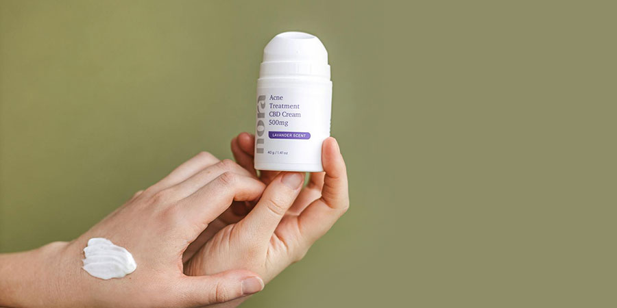 close up view of a small round white bottle of Nora CBD cream on top of a person's hand