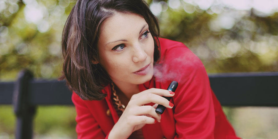 a woman with short black hair wearing a red blazer while vaping